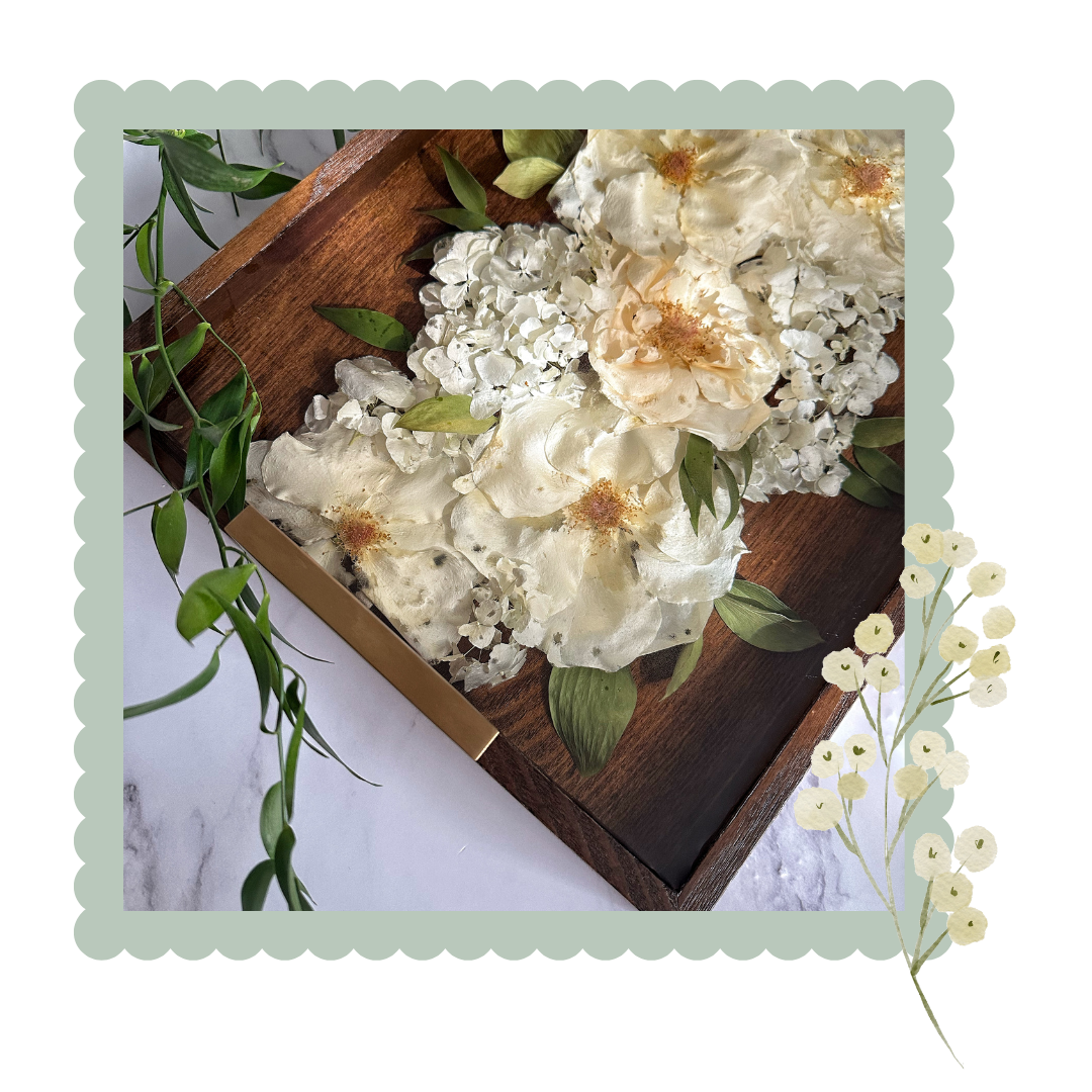 White flowers preserved in resin on a wooden tray with green leaves on a white background