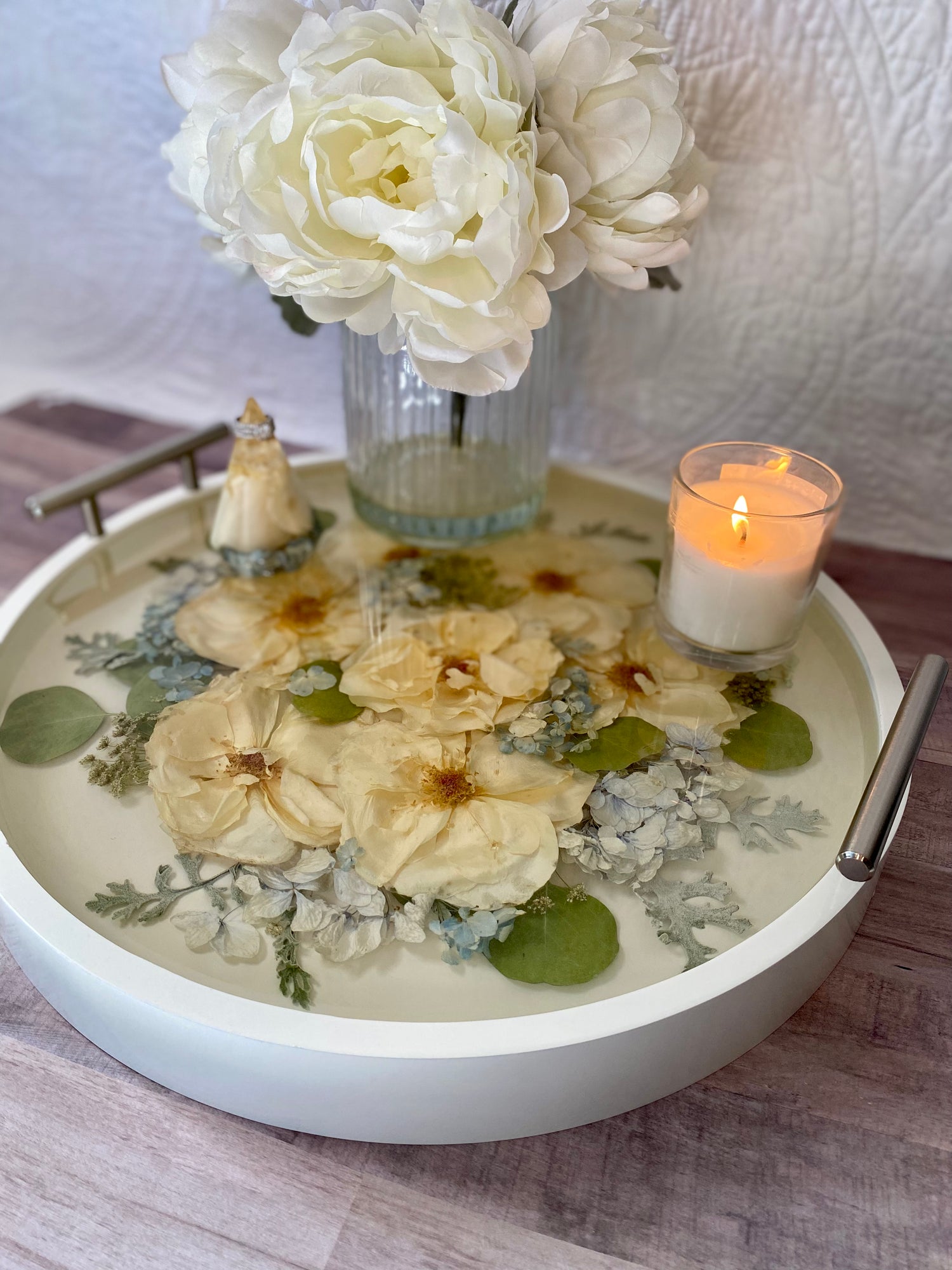 Decorative tray with flowers, a candle, and small figurines on a wooden surface.