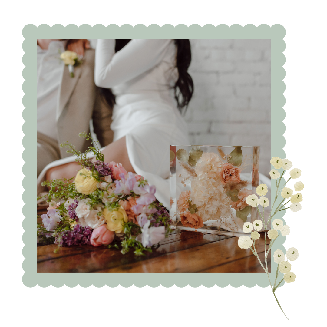 Floral resin arrangement with a couple in the background, framed with decorative elements.