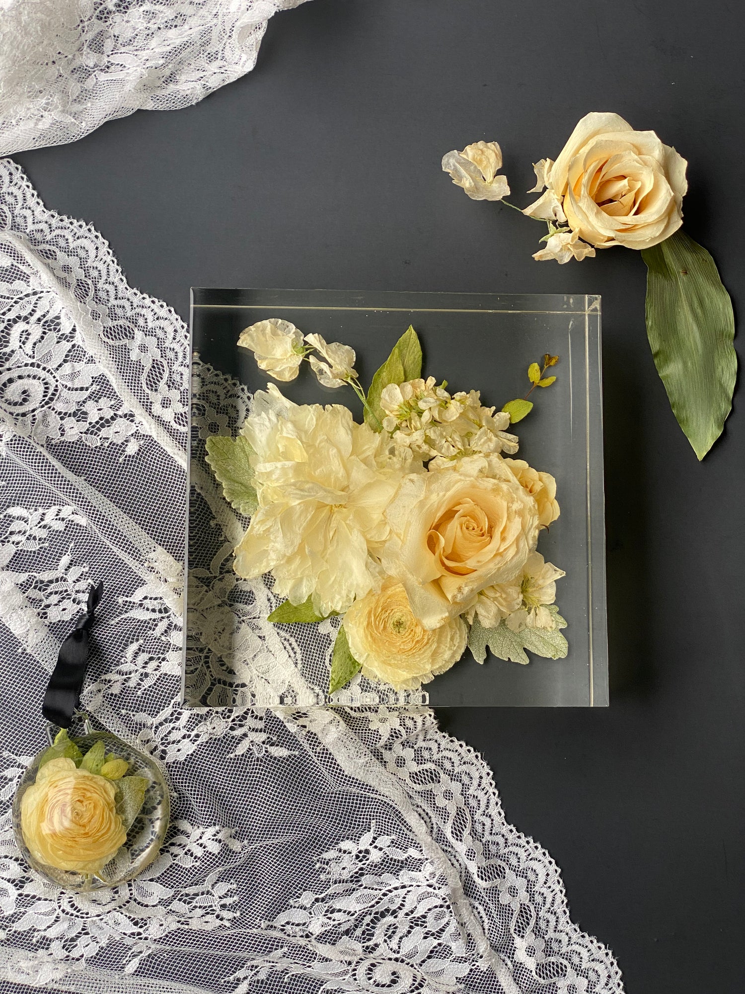 Preserved yellow roses in a resin preserved box on a black background with lace fabric.