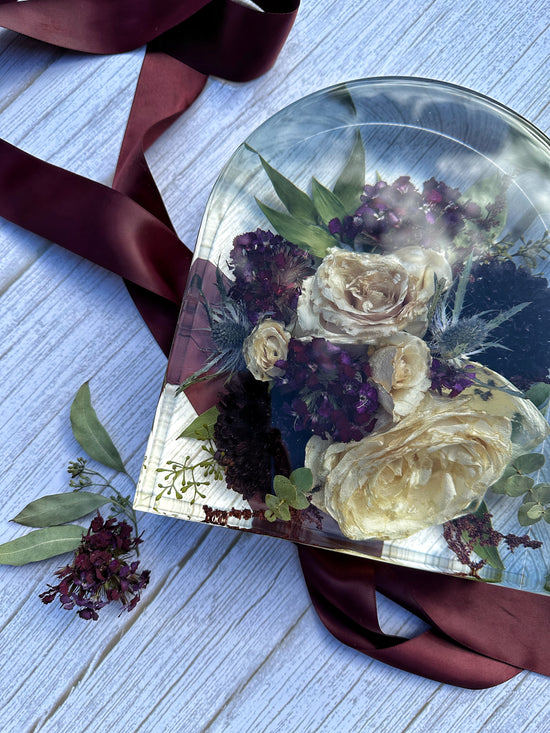 Arch-shaped resin box with preserved flowers on a wooden surface with ribbons.