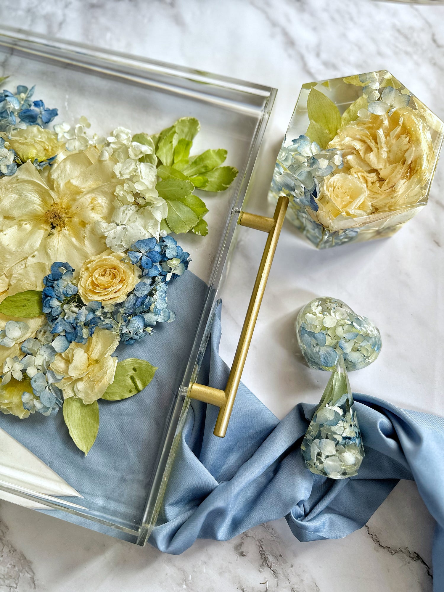 Decorative resin tray with floral design, gold handle, and blue cloth on a marble surface