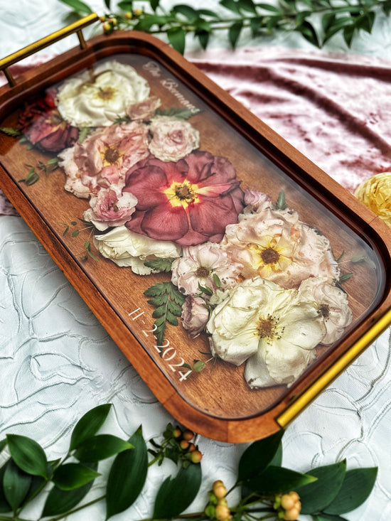 Decorative resin tray with pressed flowers and a wooden border on a light background and greenery.