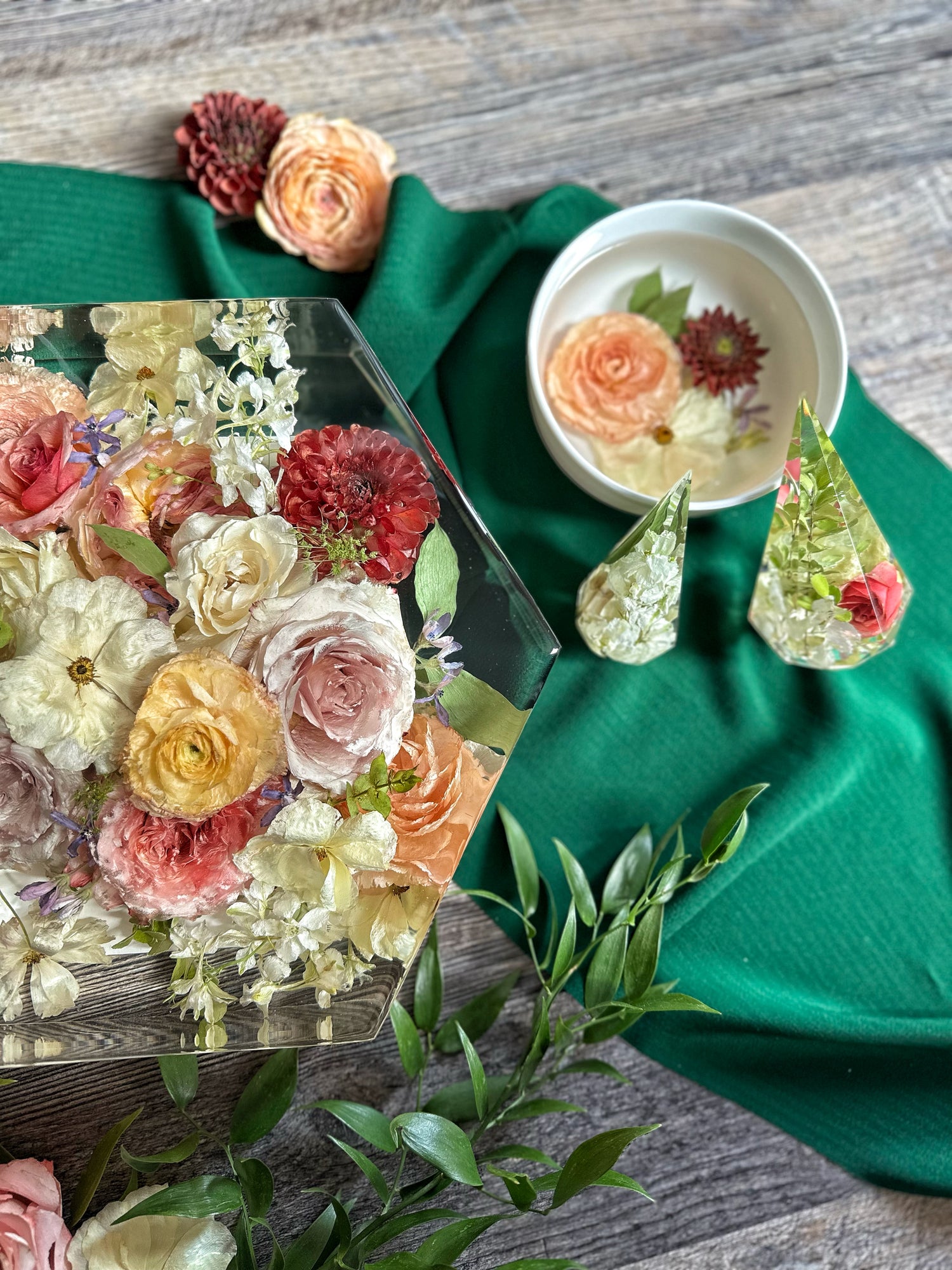 Decorative flowers in a resin hexagon, a bowl with floral design, and decorative items on a green cloth.