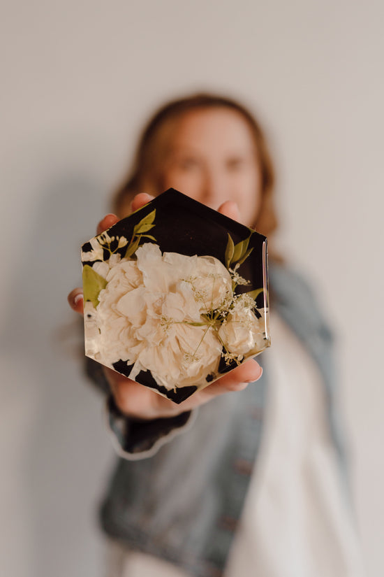 Person holding a resin floral preserve hexagon with floral design against a neutral background