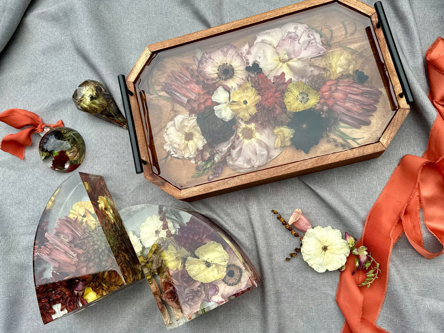Decorative resin tray with pressed flowers on a gray surface with ribbons and decorative resin accessories.