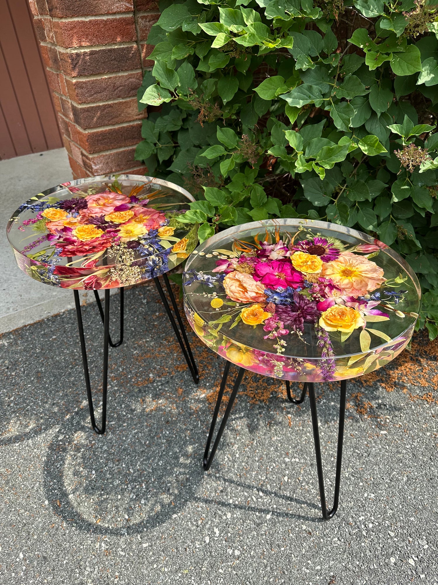 Two small round tables with resin floral preservation on a pavement.