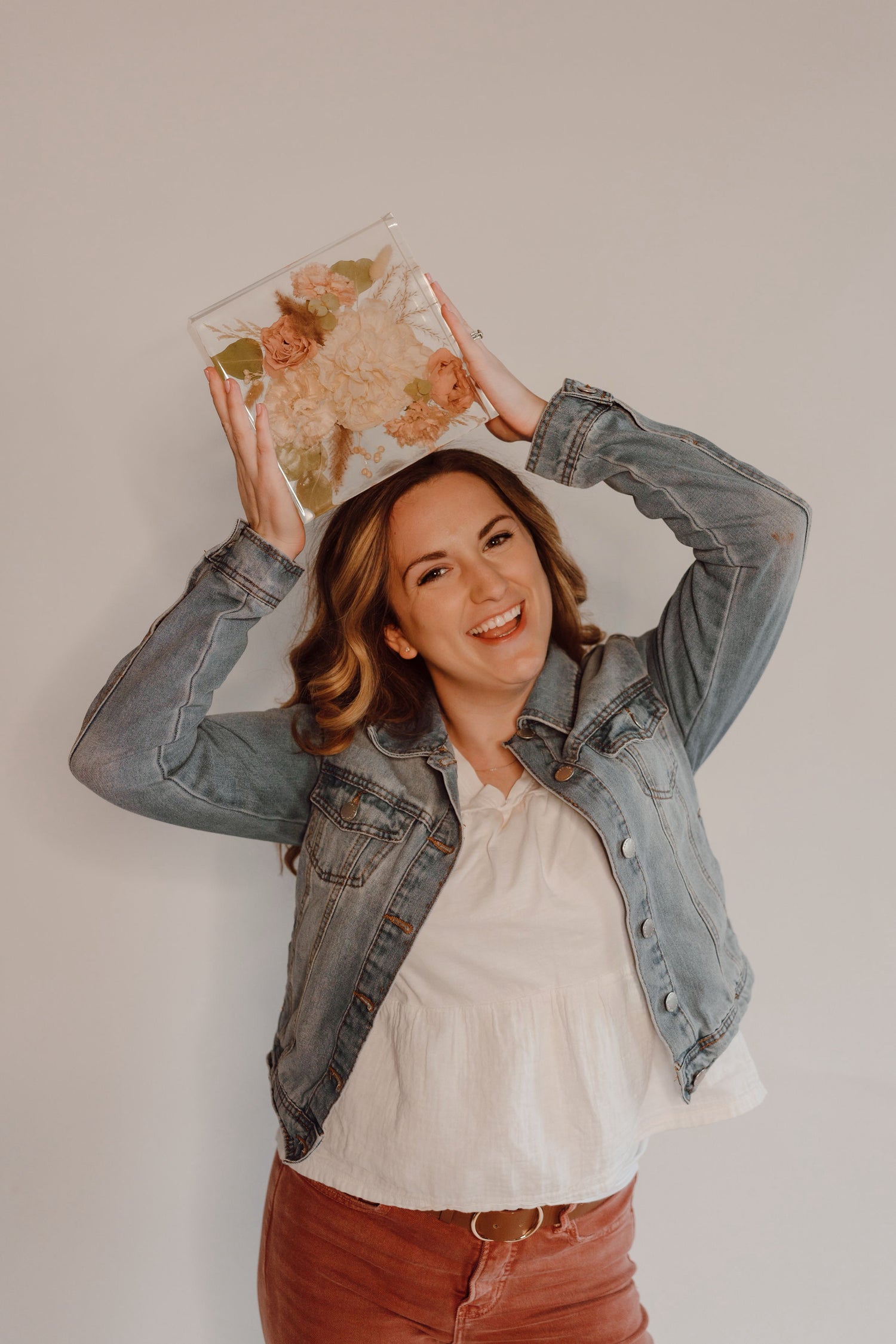 Woman holding a resin floral arrangement above her head against a plain background